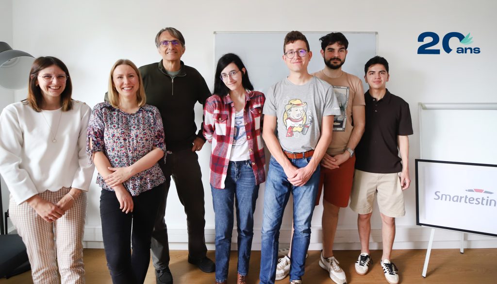 Groupe d'hommes et femmes d'âges divers, debout à côté d'un tableau blanc.