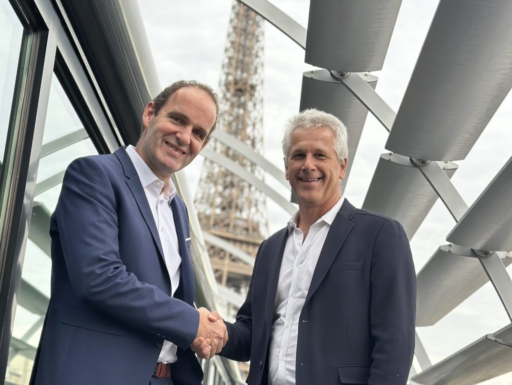 deux hommes souriants se serrent la main devant la tour eiffel