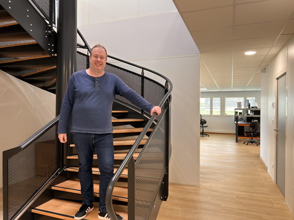 Homme blanc souriant devant un escalier de bureau